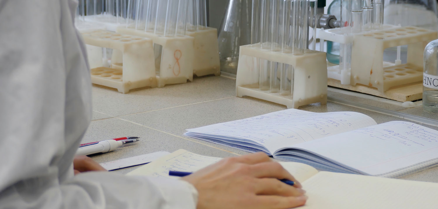 Scientist taking notes in a lab with test tubes in the background, representing documentation and mistakes in medical lab results.