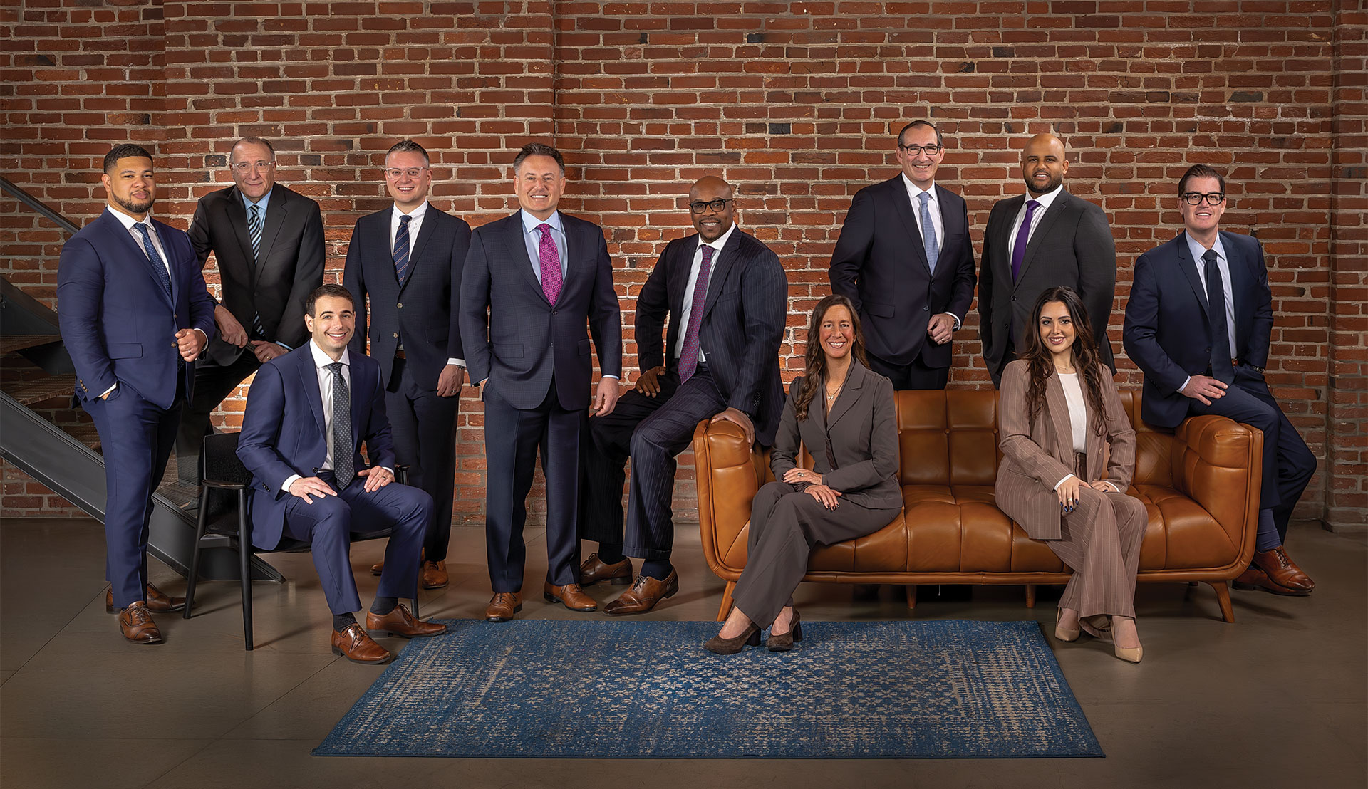 A group of attorneys standing and sitting in an open room in front of a brick wall smiling